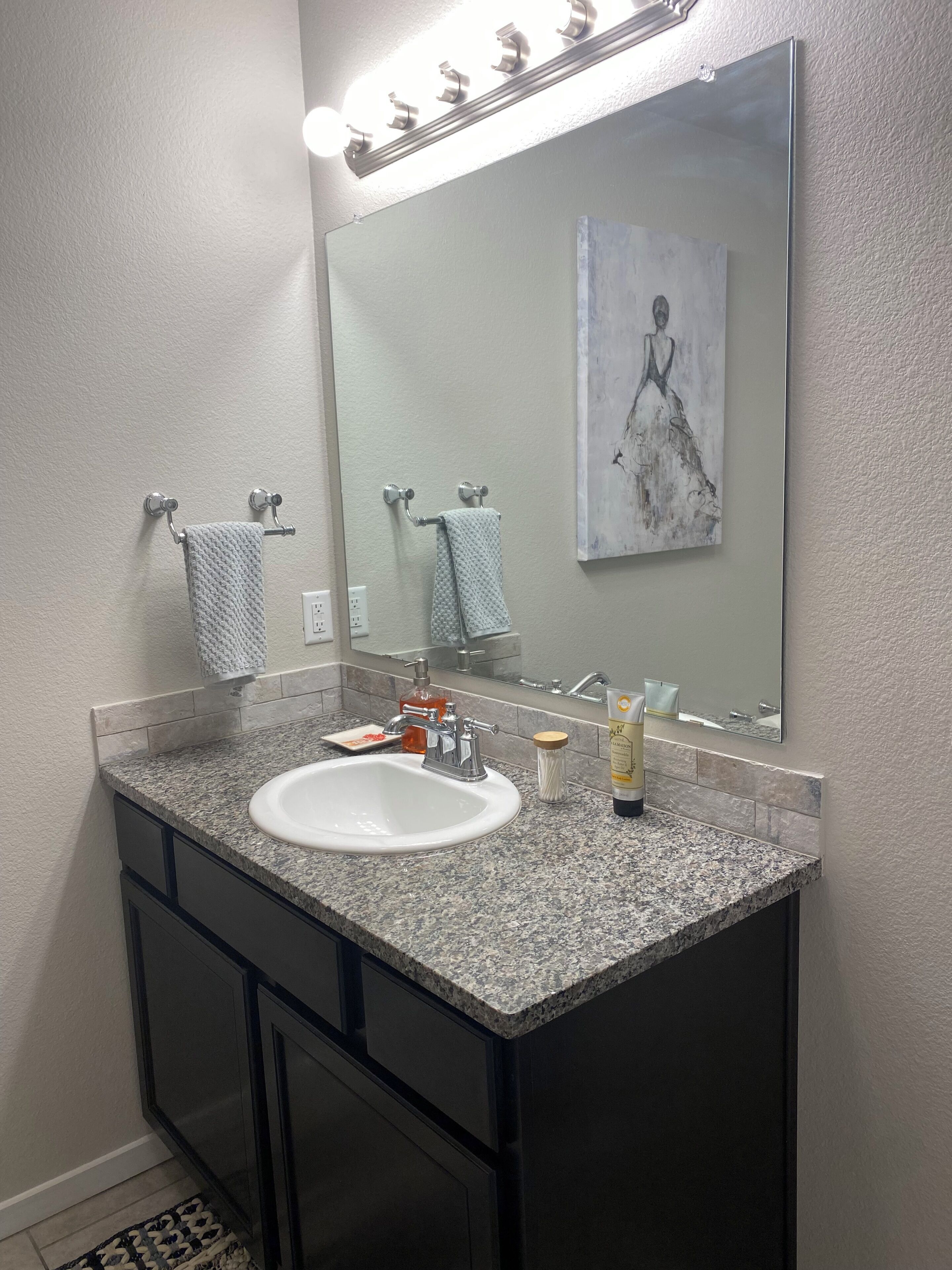 A bathroom with a granite countertop sink, a large mirror, and a painting above the mirror.