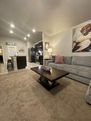 A modern living room with a sofa, a coffee table, and a kitchen area in the background.