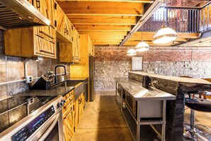 A kitchen with wooden cabinets, stainless steel appliances, and a stone wall. - The Lions Lair - New loft style home in STL (St. Louis)