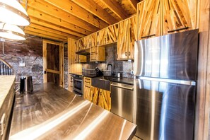 A modern kitchen with wooden cabinets, stainless steel appliances, and a stone wall. - The Lions Lair - New loft style home in STL (St. Louis)