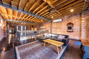 A spacious loft with exposed wooden beams, a brick wall, a leather sofa, and a leopard print rug. - The Lions Lair - New loft style home in STL (St. Louis)