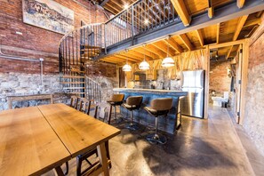 A rustic interior with a wooden staircase, a kitchen area, and a dining space with bar stools. - The Lions Lair - New loft style home in STL (St. Louis)