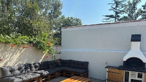Un patio exterior amb una banca de fusta, un sofà negre i una barbacoa.