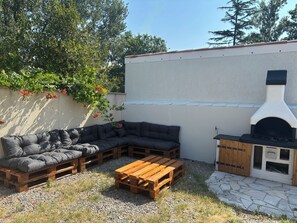 An outdoor patio with a wooden bench, a black sofa, and a barbecue grill. - Quiet house with a pool and garden (Mérignac)
