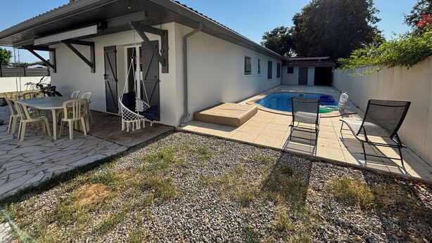 Una casa amb un pati, una cadira penjant, una piscina i una taula amb caires.