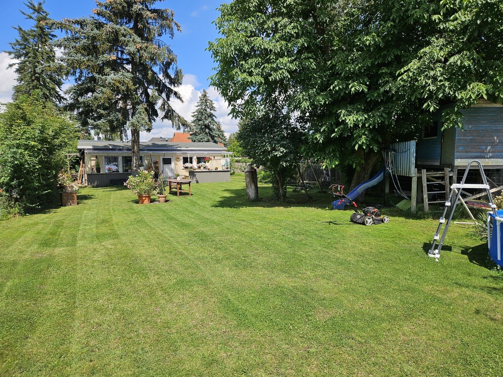 Un jardin avec une pelouse, un espace de jeux doté d’un toboggan et une maison avec un abri de jardin.