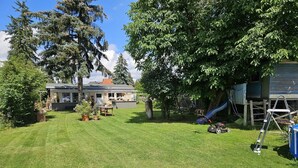 Un patio trasero con césped, una zona de juegos con un tobogán y una casa con un cobertizo.