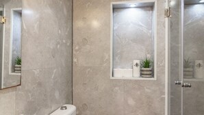 Un baño con inodoro, lavamanos, ducha y una pequeña ventana con una planta.