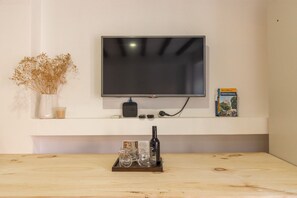 A flat-screen TV mounted on a white wall, a small table with a bottle and glasses, a vase with dried flowers, and a book titled 'Portugal' on the wall. - Bairro Alto Studio 2 · Right in the Heart of the City · AC (Lisboa)