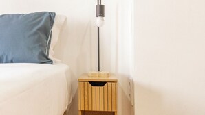 Un dormitorio con una cama, una mesita de noche con lámpara y una mesita auxiliar de madera.