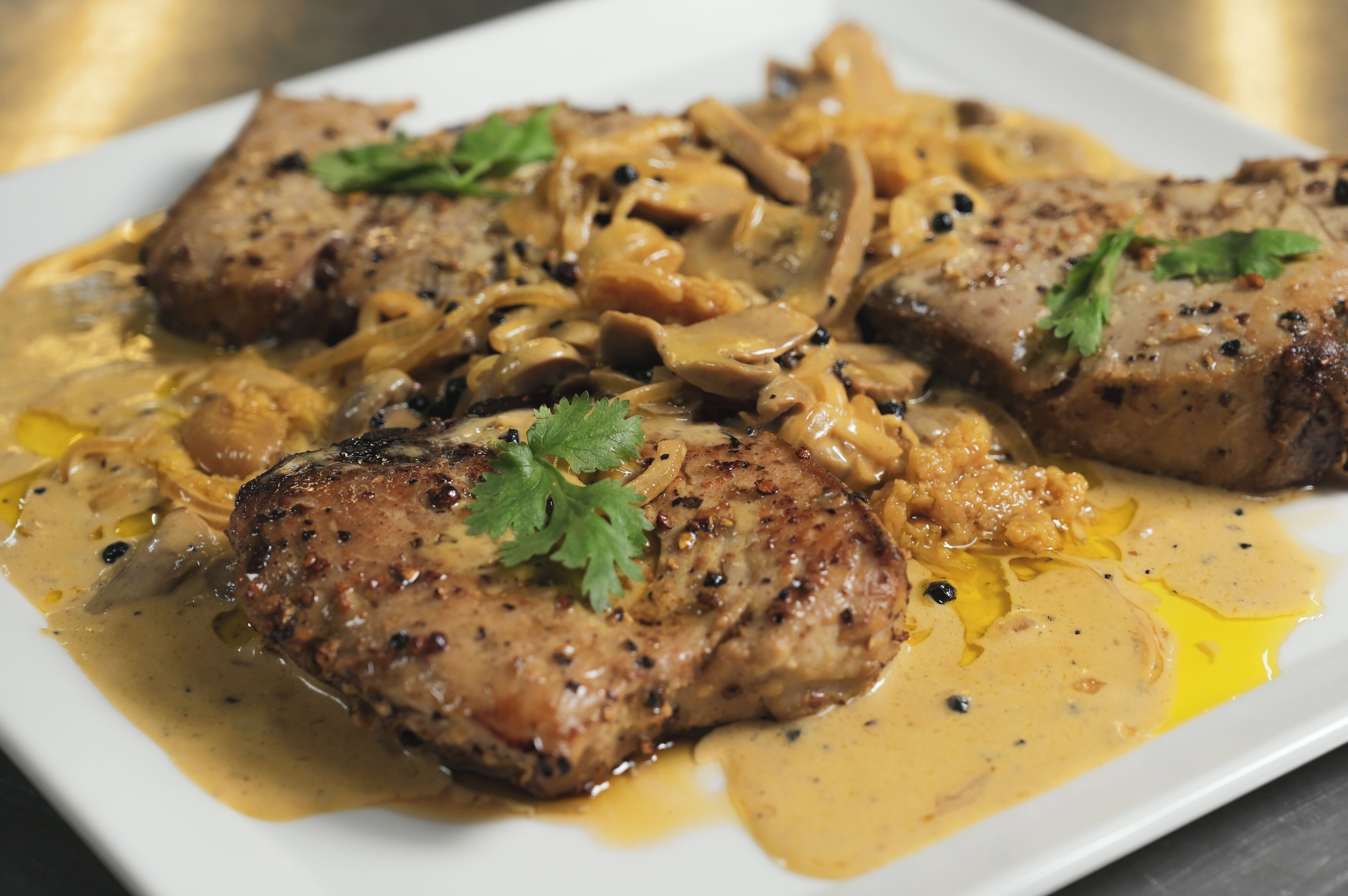 Un plato de comida con carne a la parrilla y champiñones en salsa cremosa, adornado con perejil.
