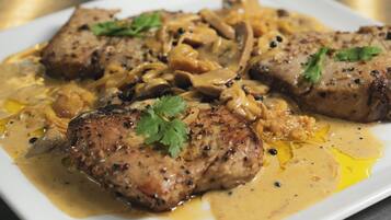 Un plato de comida con carne a la parrilla y champiñones en salsa cremosa, adornado con perejil.