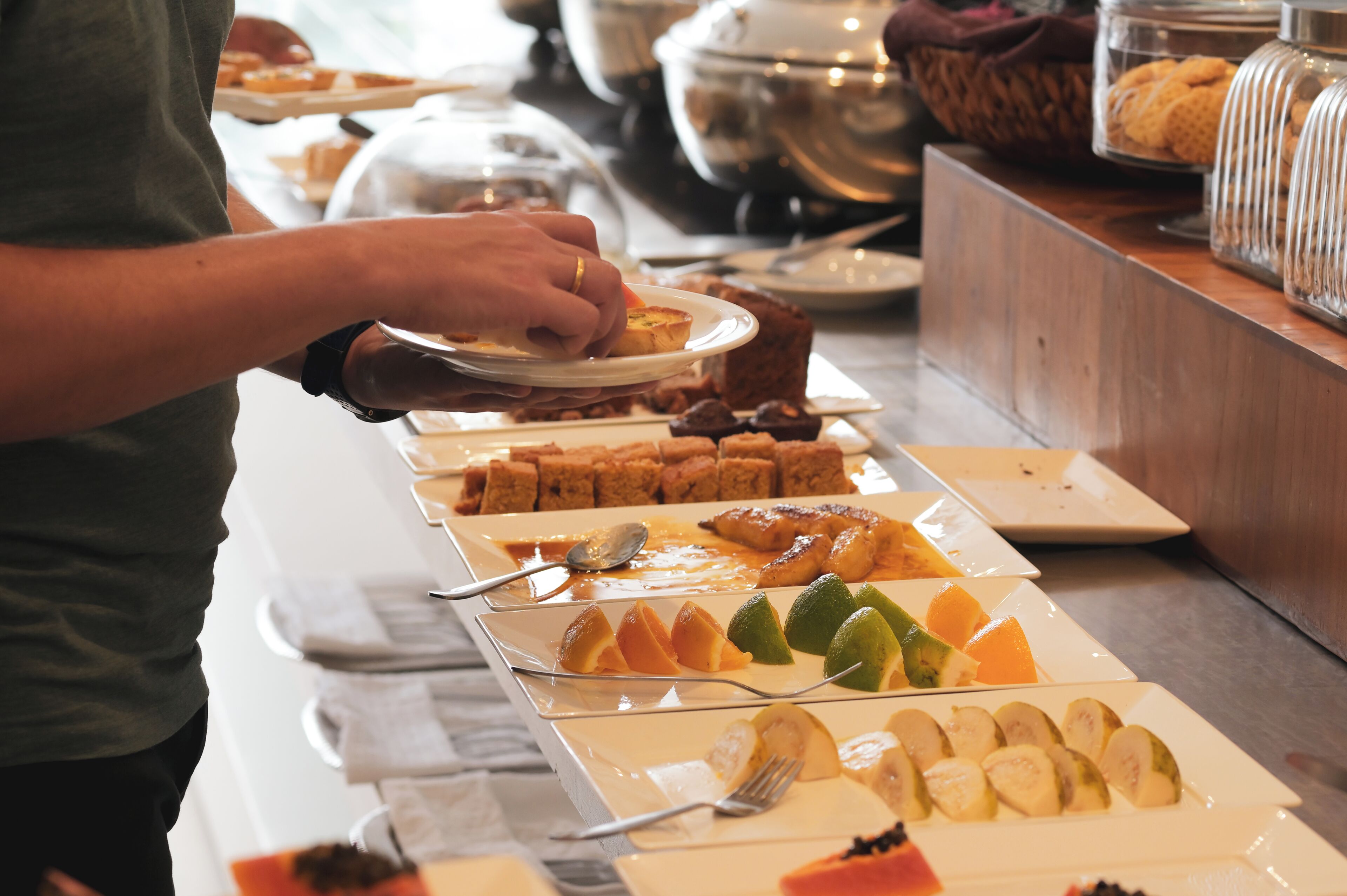 A buffet setup with various food items and a person serving themselves.