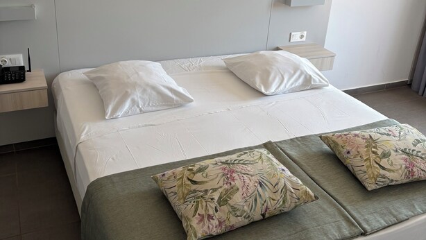 Une chambre d’hôtel avec un lit, deux oreillers, une table de chevet et une petite table.
