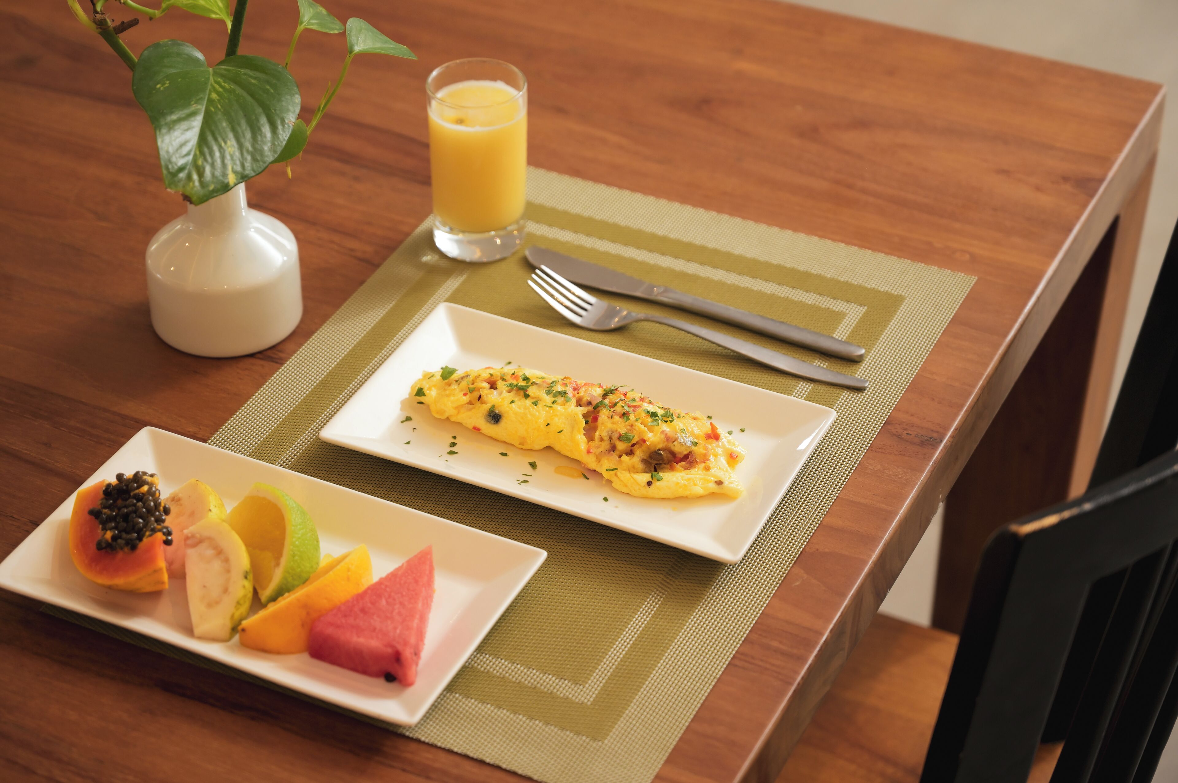 A breakfast setting with an omelette, fruit, and orange juice on a wooden table.