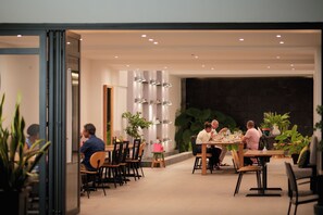 Un espace repas moderne doté de plusieurs tables et chaises, d’un éclairage d’ambiance et de plantes d’intérieur.
