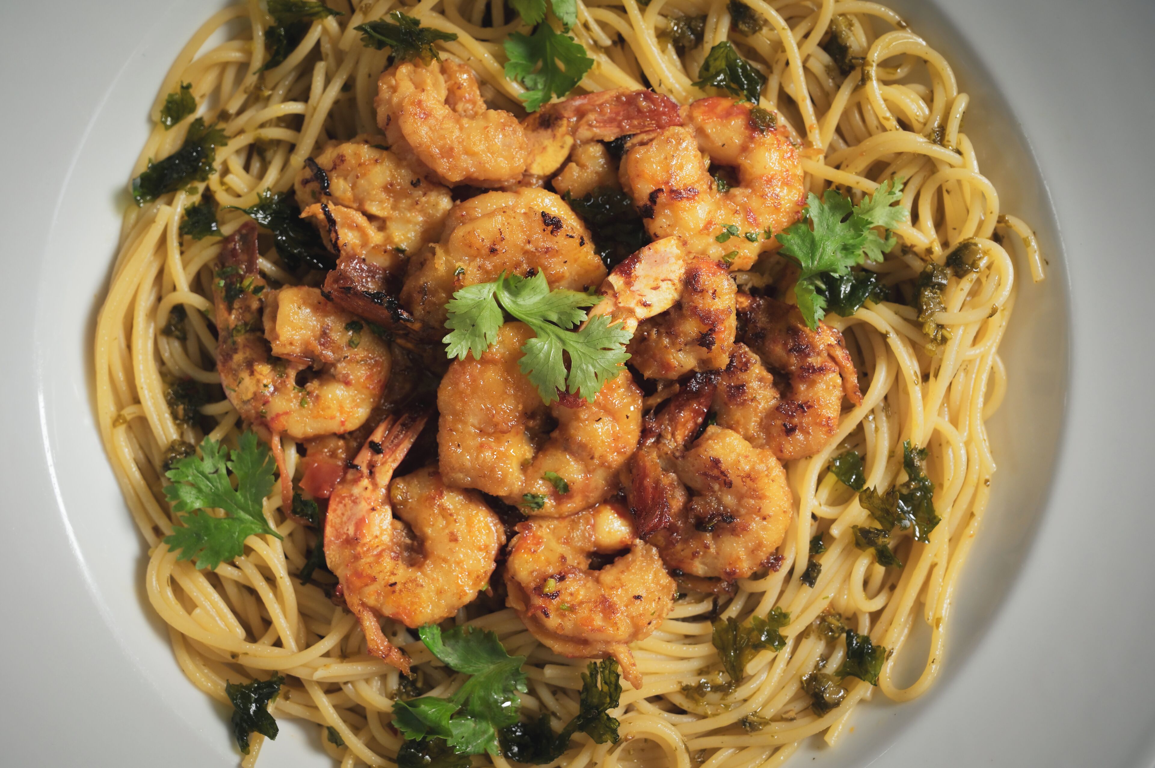 Un plato de espagueti con camarones y hierbas para decorar.