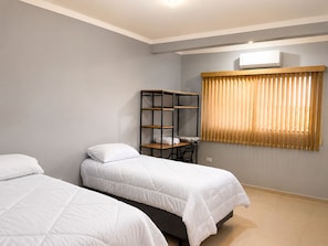 Habitación de hotel con dos camas, un escritorio, una silla, una ventana con persianas y un equipo de aire acondicionado.