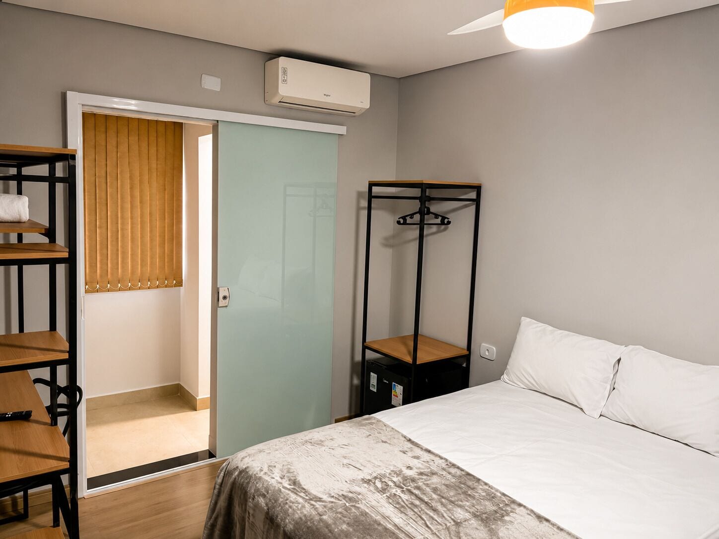 A bedroom with a bed, a wardrobe, a shelf unit, and a hanging rack.