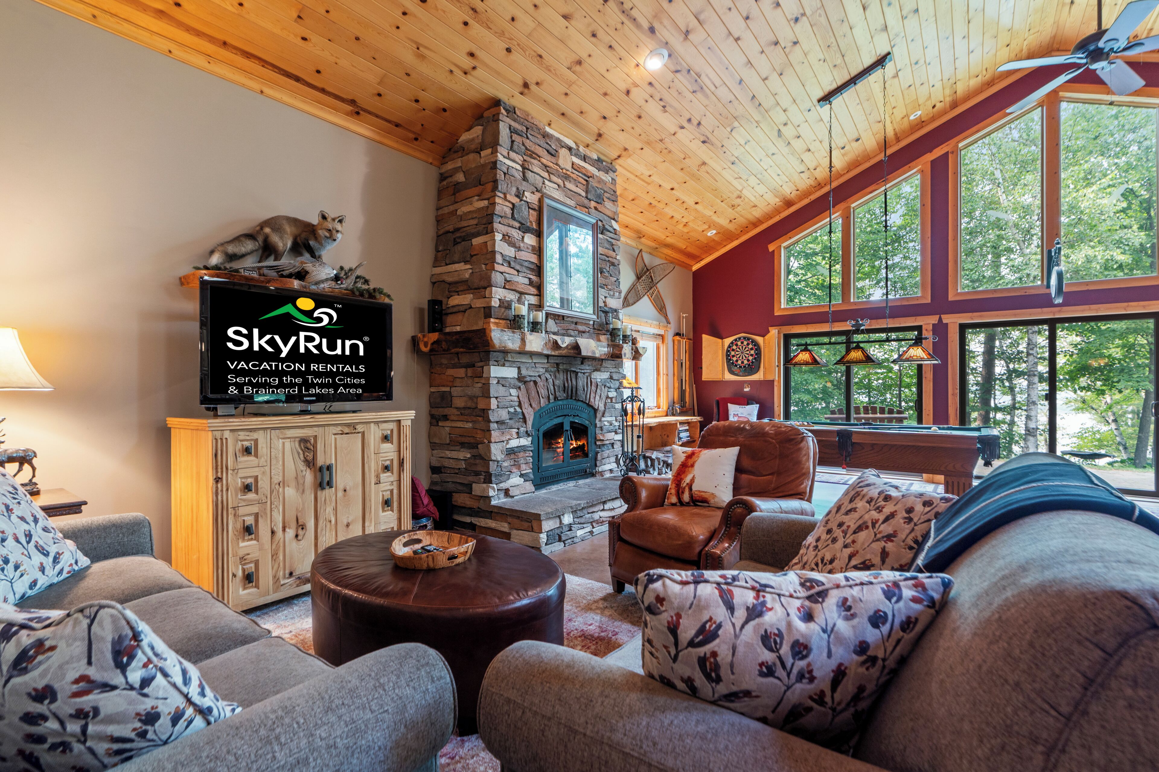 Una sala de estar acogedora con chimenea de piedra, mobiliario de cuero y ventanas amplias.