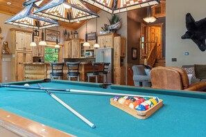 Ein Billardtisch mit Billardkugeln und Spielstöcken, Holzschränke, ein Kamin und ein aufgehängter Tierkopf.