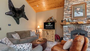 A cozy living room with a stone fireplace, a mounted bear hide, and a television displaying SkyRun. - Handcrafted 4BR Cabin on Rabbit Lake, Aitkin (Aitkin)