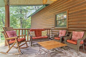 A log cabin with a porch, furnished with a rocking chair, two sofas, and a coffee table.