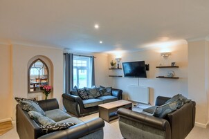 A living room with a sofa set, a coffee table, a flat-screen TV mounted on the wall, and a radiator.