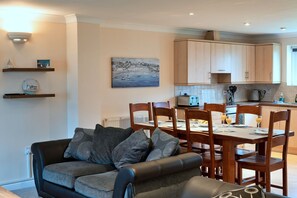 A modern living room with a sofa and chairs, a dining table with chairs, and a kitchen area with wooden cabinets. - Contemporary Cornwall Retreat for Groups (St. Columb Major)
