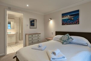 A hotel room with a bed, a nightstand, a dresser, a painting, and a bathroom with a sink and shower.