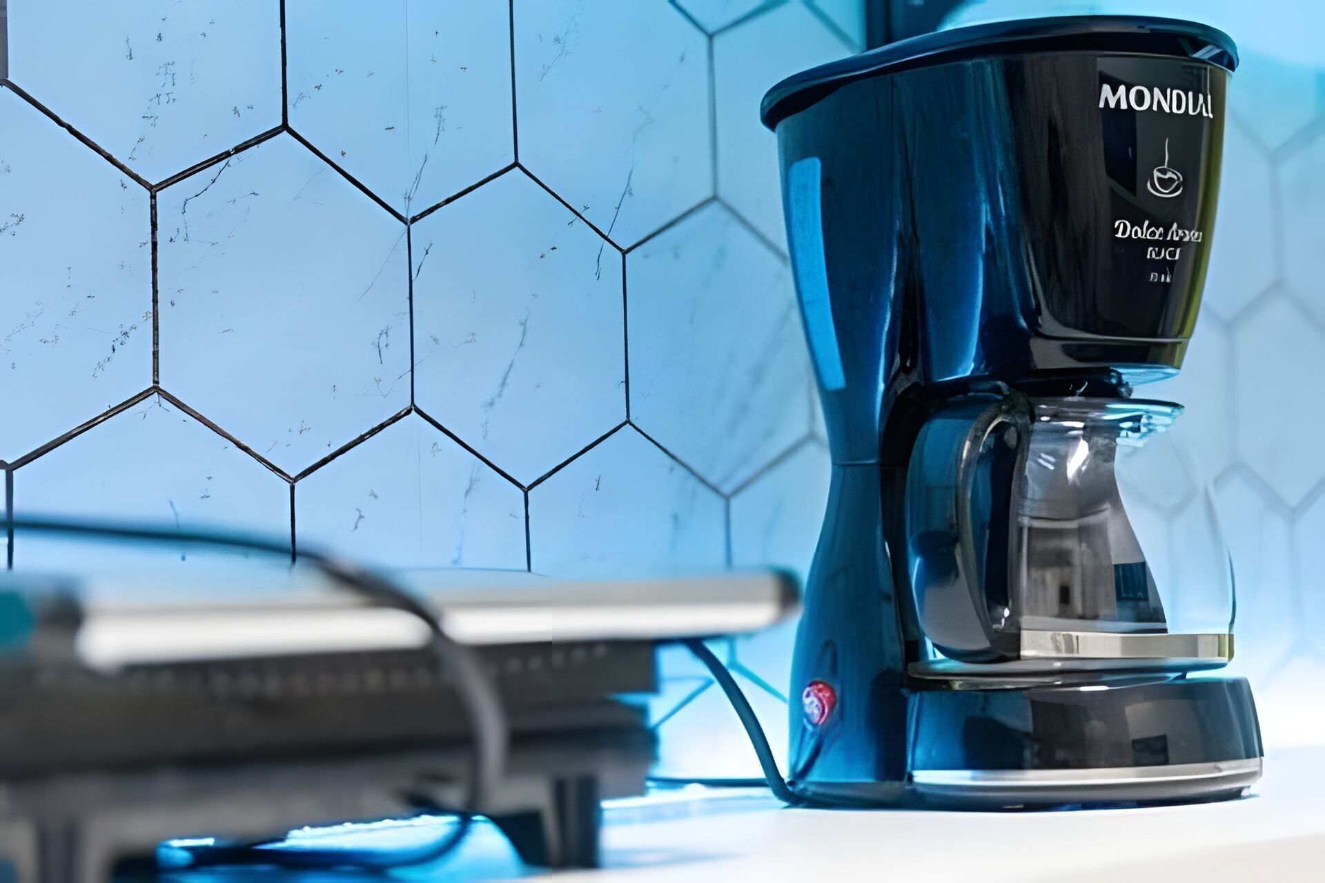 A coffee maker with a label, placed on a counter with a tiled backsplash.
