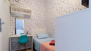 Une petite chambre avec un bureau, une chaise, un lit et une fenêtre.