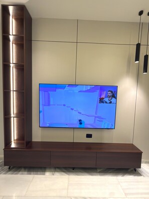 A flat-screen TV mounted on a wall with a wooden cabinet below. - Luxury 3-Bedroom Family Apartment, Prime Location, Free WiFi & Free Parking (Amman)
