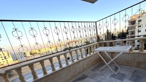 A balcony with a metal railing, a table, and a view of buildings and a road. - Luxury 3-Bedroom Family Apartment, Prime Location, Free WiFi & Free Parking (Amman)