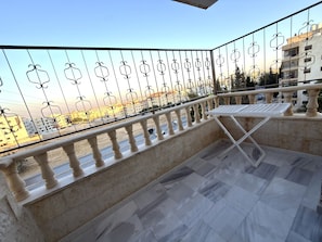 A balcony with a metal railing, a table, and a view of buildings and a road. - Luxury 3-Bedroom Family Apartment, Prime Location, Free WiFi & Free Parking (Amman)