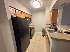 A compact kitchen with a black refrigerator, wooden cabinets, a stainless steel sink, and a trash can. - Exceptional Location - Downtown DC, Walk to Shops, Rooftop Pool, Jacuzzi, Gym (Washington)