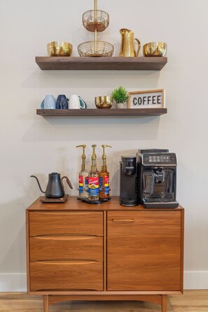 A coffee station with a coffee maker, Torani syrup, and a sign that says 'COFFEE'. - Mid-Century Modern Retreat with Hot Tub (Branson)