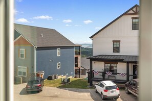 A residential area with houses, a driveway, parked cars, and a clear view of a body of water in the distance. - Mid-Century Modern Retreat with Hot Tub (Branson)