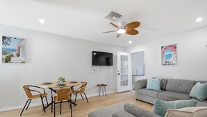 A modern living room with a grey sofa, a dining table with chairs, a ceiling fan, and a flat-screen TV mounted on the wall. - BC-8-person 4-bedroom 2 bath/Triplex in Downton Naples close to the Beach 5th Av (Naples)