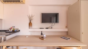 Een moderne keuken met een flatscreen televisie aan de muur, een houten eettafel met stoelen, en een klein plankje met een vaas en flessen.