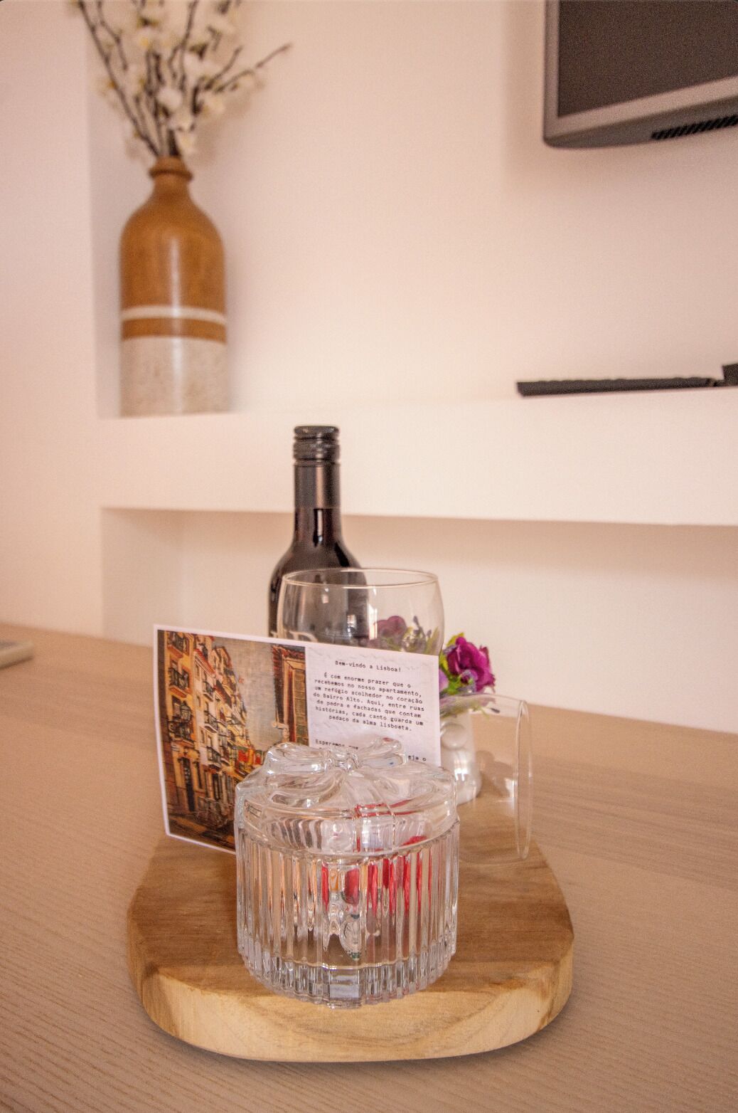 A wooden table with a glass decanter, a glass bottle, a card with text, and a vase with flowers.