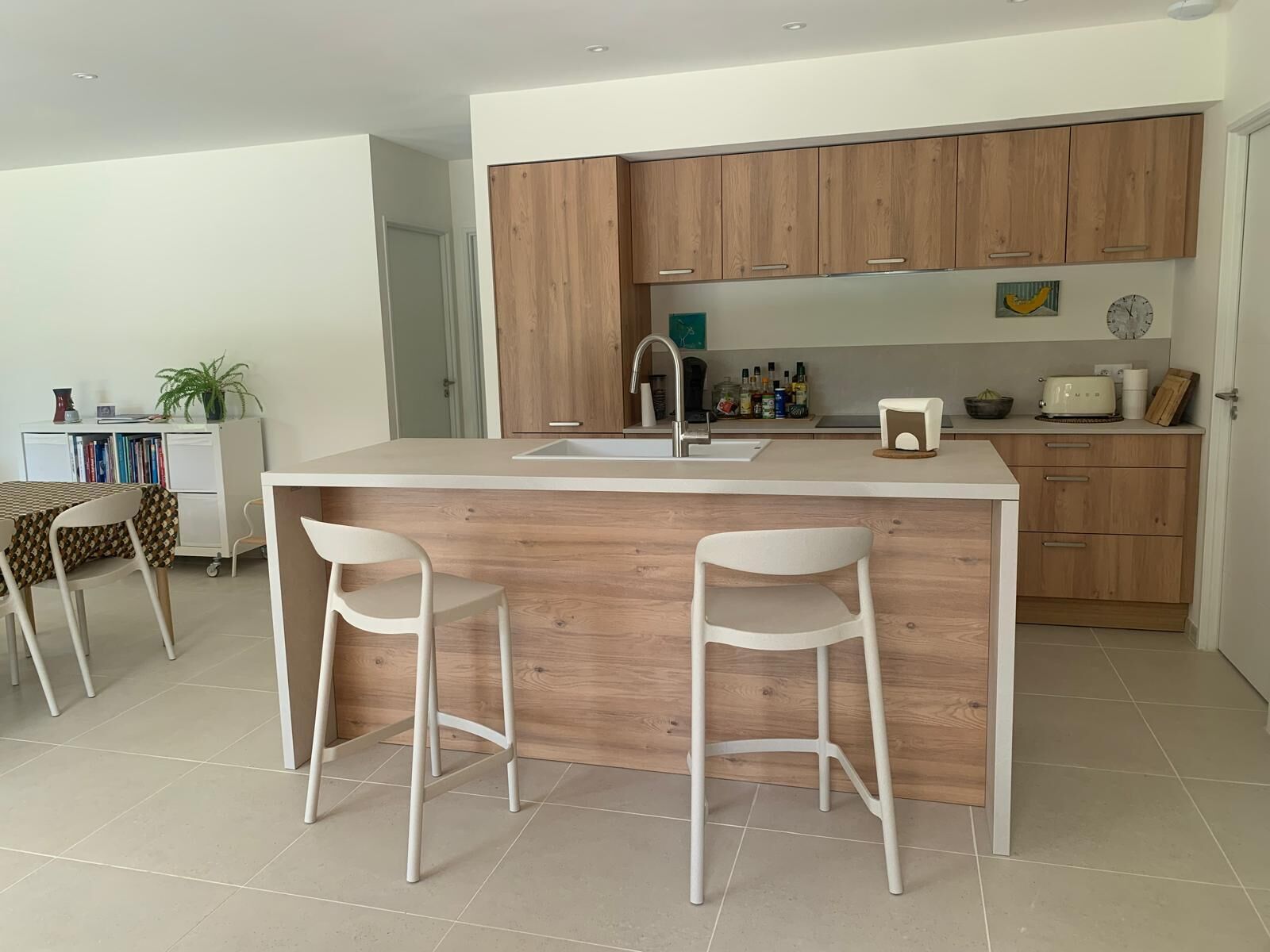 A modern kitchen with wooden cabinets, a central island with stools, a white countertop, and a sink.
