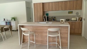 Een moderne keuken met houten kastjes, een centraal eiland met krukken, een wit aanrecht en een spoelbak.