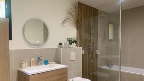 Een moderne badkamer met een houten wastafelmeubel, een ronde spiegel, een toilet en een douchecabine.