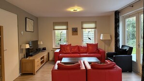 A modern living room with a red sofa set, a wooden cabinet, a television, and a dining table. - 3-bed Villa With Whirlpool (De Koog)