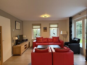 Ein modernes Wohnzimmer mit einer roten Sofagarnitur, einem Holzschrank, einem Fernseher und einem Esstisch.