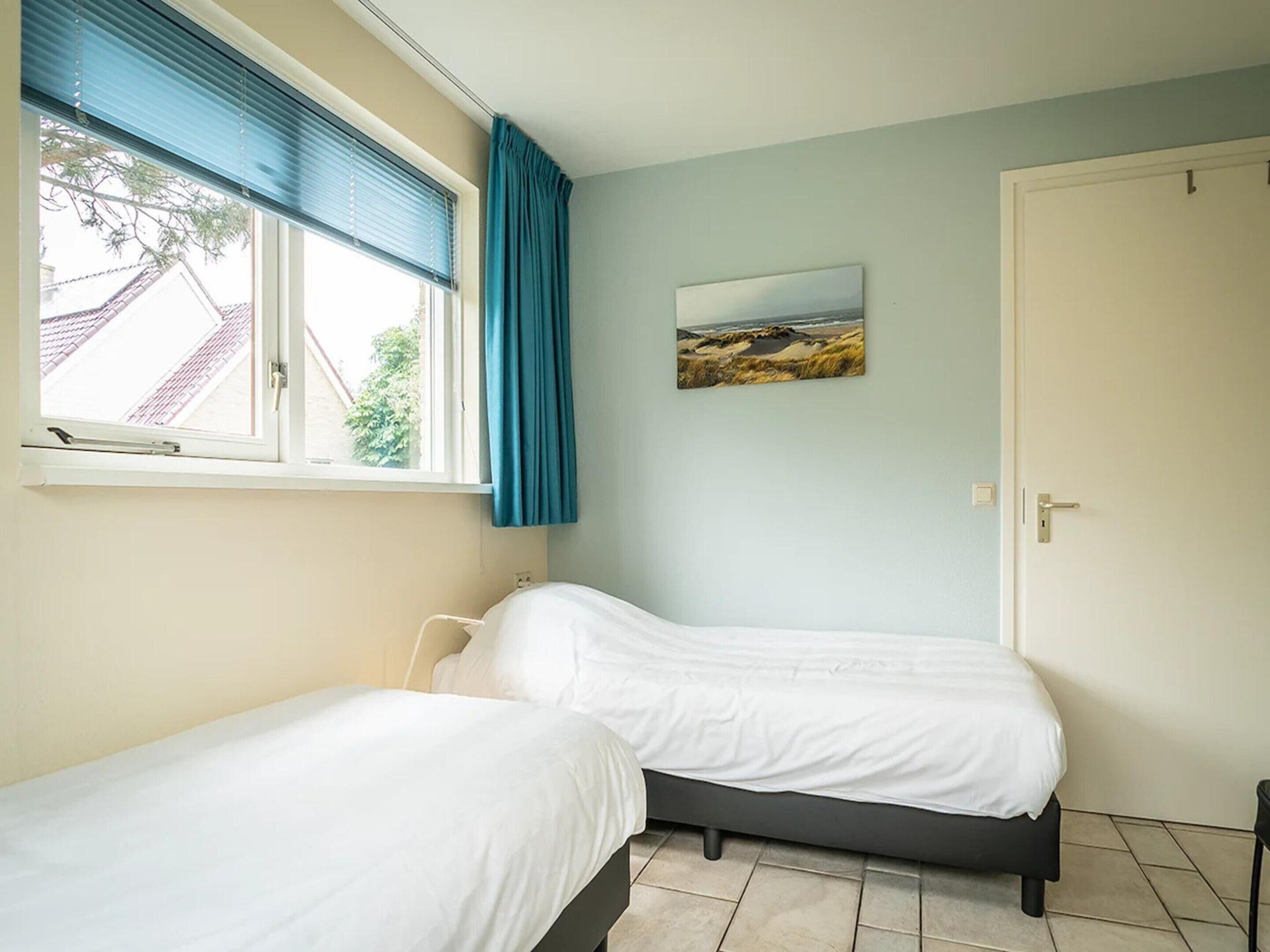 Una camera da letto con due letti, una finestra con persiane, una porta e un quadro appeso al muro.