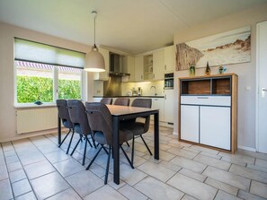 Eine moderne Küche mit Essbereich, ausgestattet mit einem Tisch, Stühlen, einer Hängeleuchte und Blick auf Grünflächen.