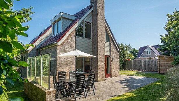 A two-story house with a brick exterior, a chimney, and a patio with outdoor furniture. - 3-bed Villa With Whirlpool (De Koog)