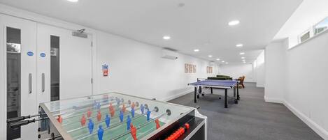 A room with a foosball table, a ping pong table, and a sofa.
